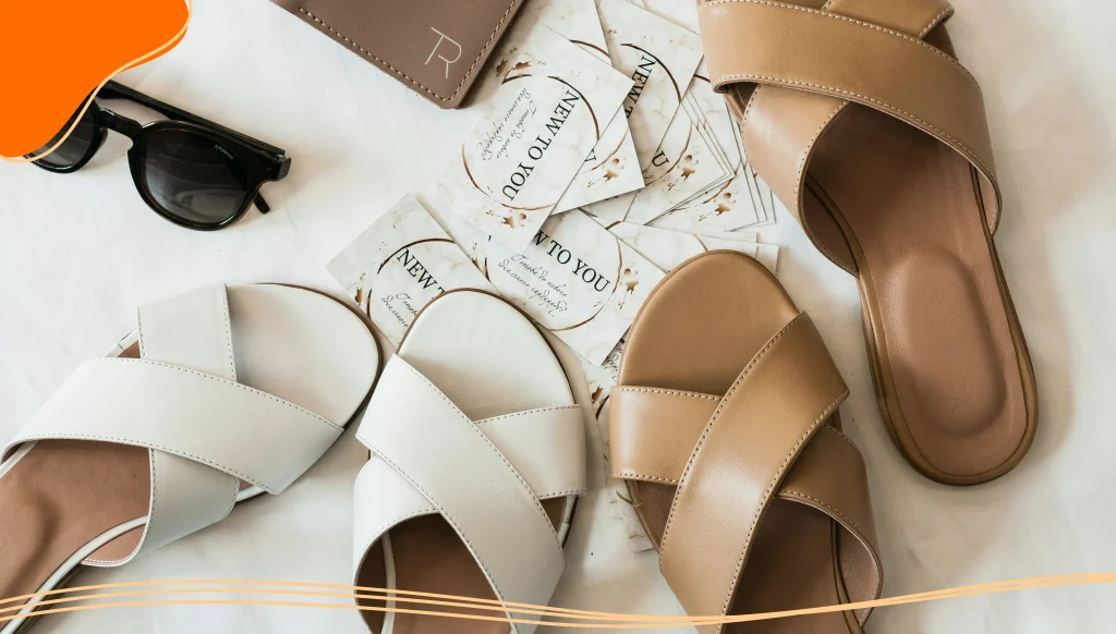 Brown leather flip flops next to black sunglasses and a pile of business cards
